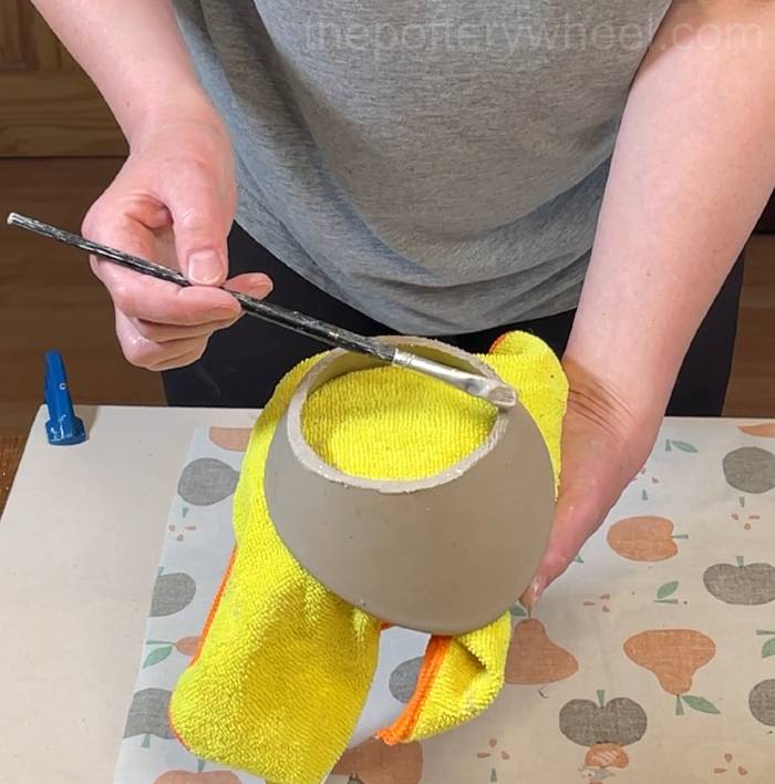 applying slip to the bottom rim of the flower jug vase